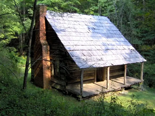 Reconstructed pioneer log cabin with stone chimney surrounded by trees and a split-rail fence